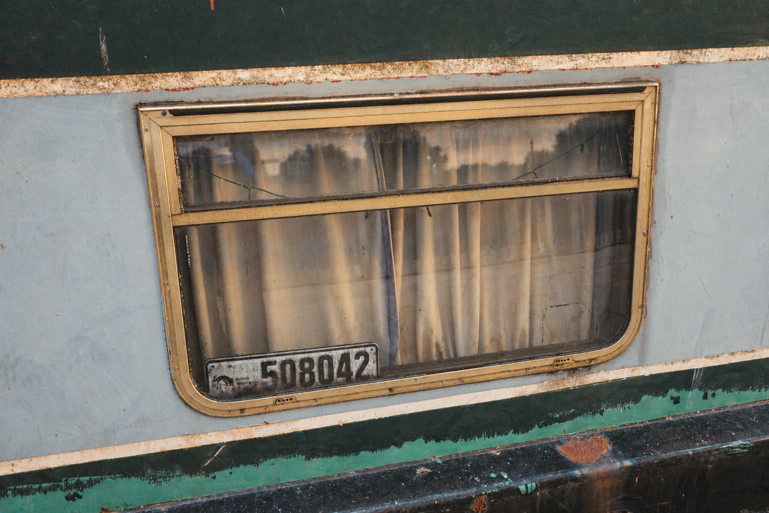 Close-up of a weathered narrowboat window with a brass frame and a registration plate