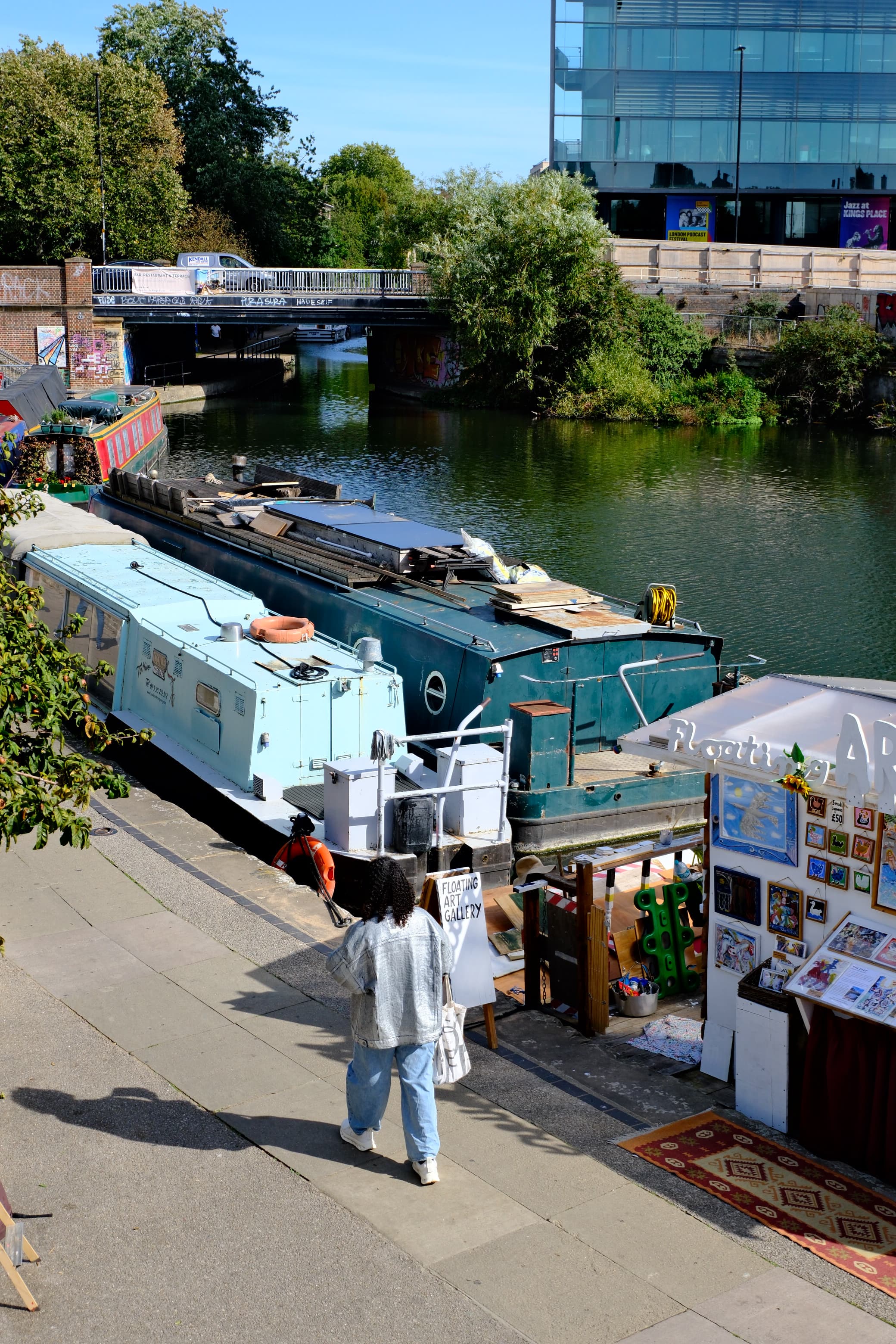 Looking down on narrowboats moored along the canal, a person in a denim jacket walking past on the towpath