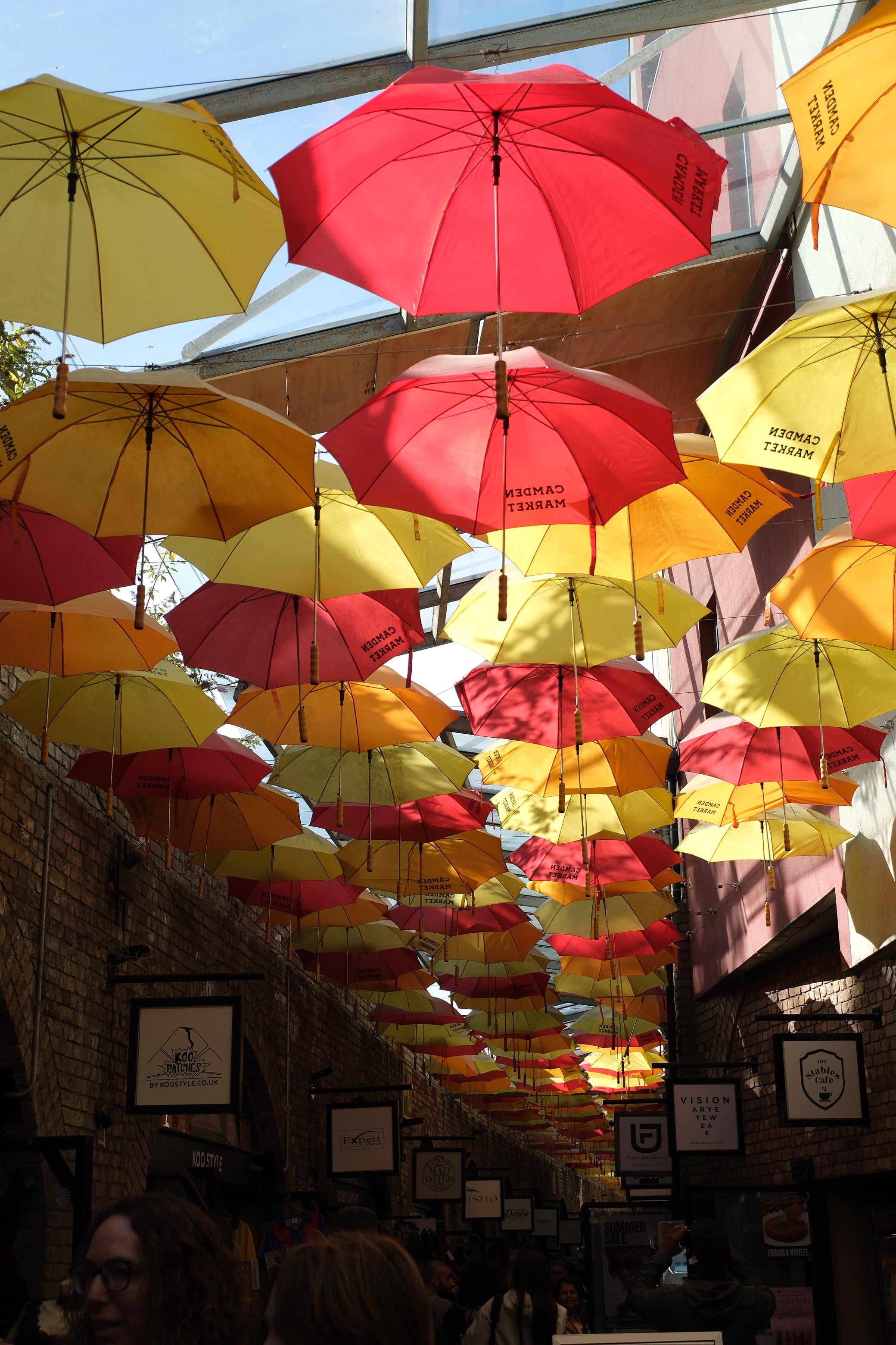 Red, orange and yellow umbrellas hanging above a covered market walkway, sunlight shining through